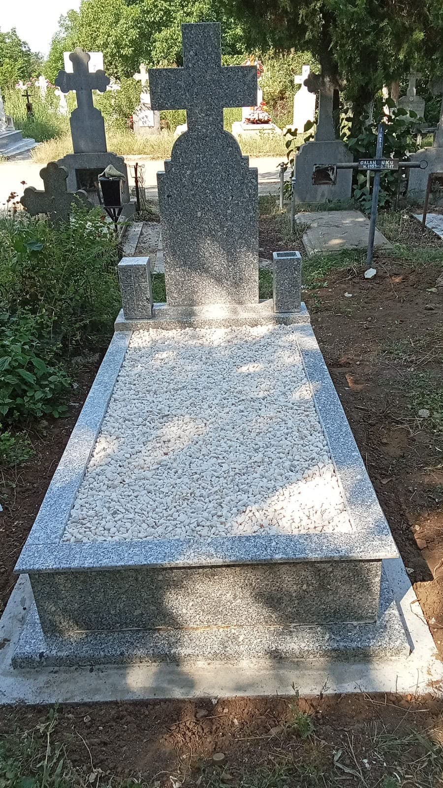 Monument din granit gri cu cruce și pietriș alb decorativ