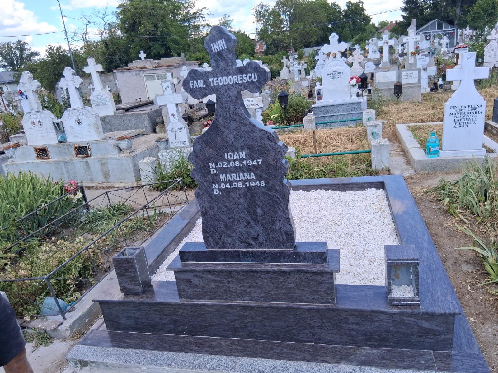 Cavou cu cruce din granit montat în cimitir, cu pietriș alb decorativ